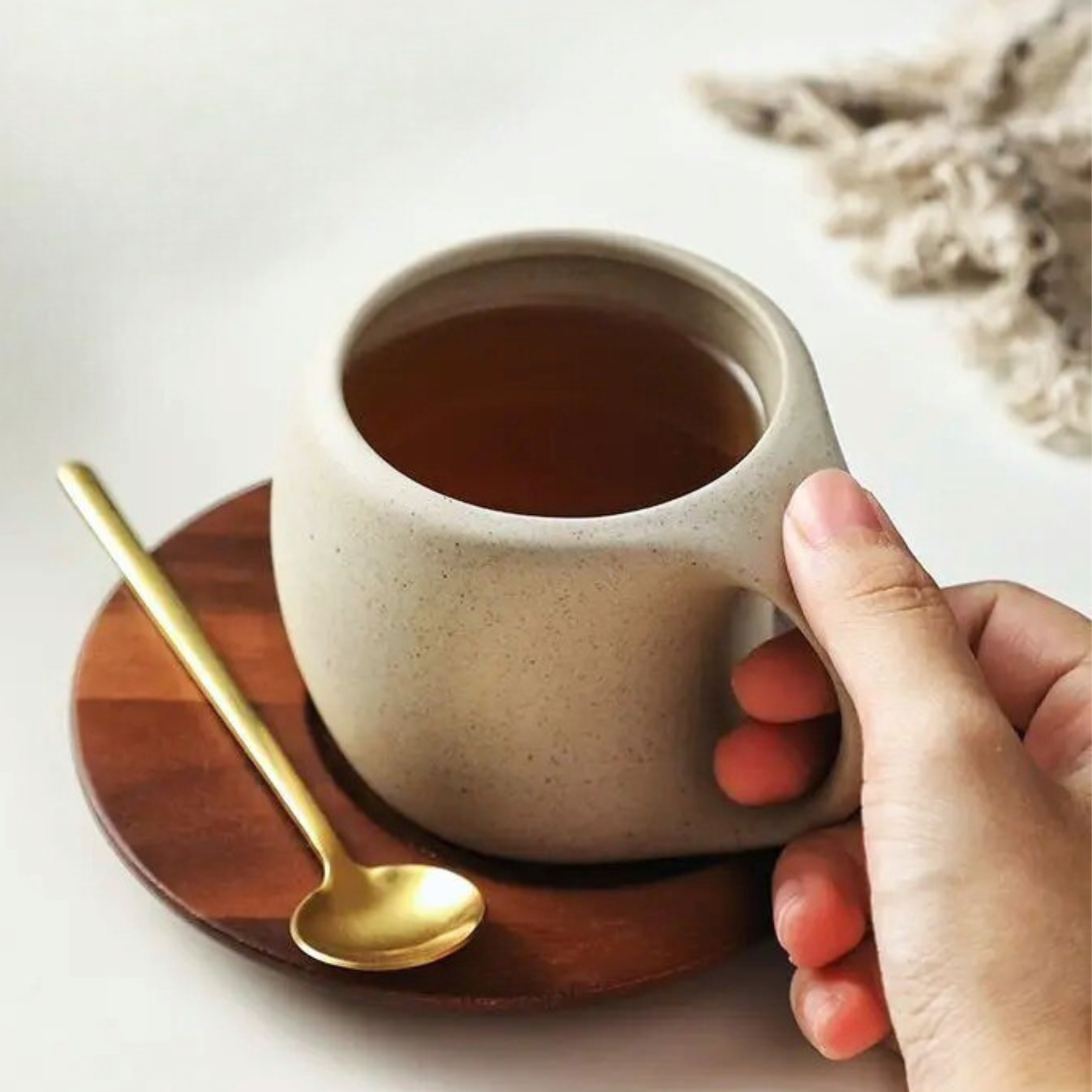 Close-up of ceramic cup and gold-tone spoon on wooden base, focusing on textures and finish