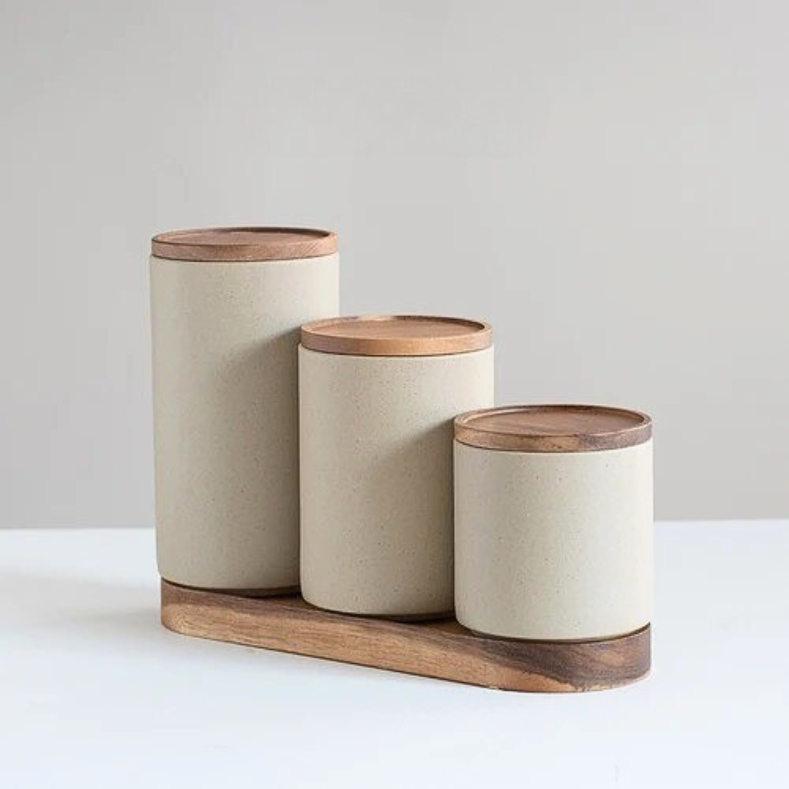 Set of three ceramic storage jars in different sizes placed on matching wooden bases