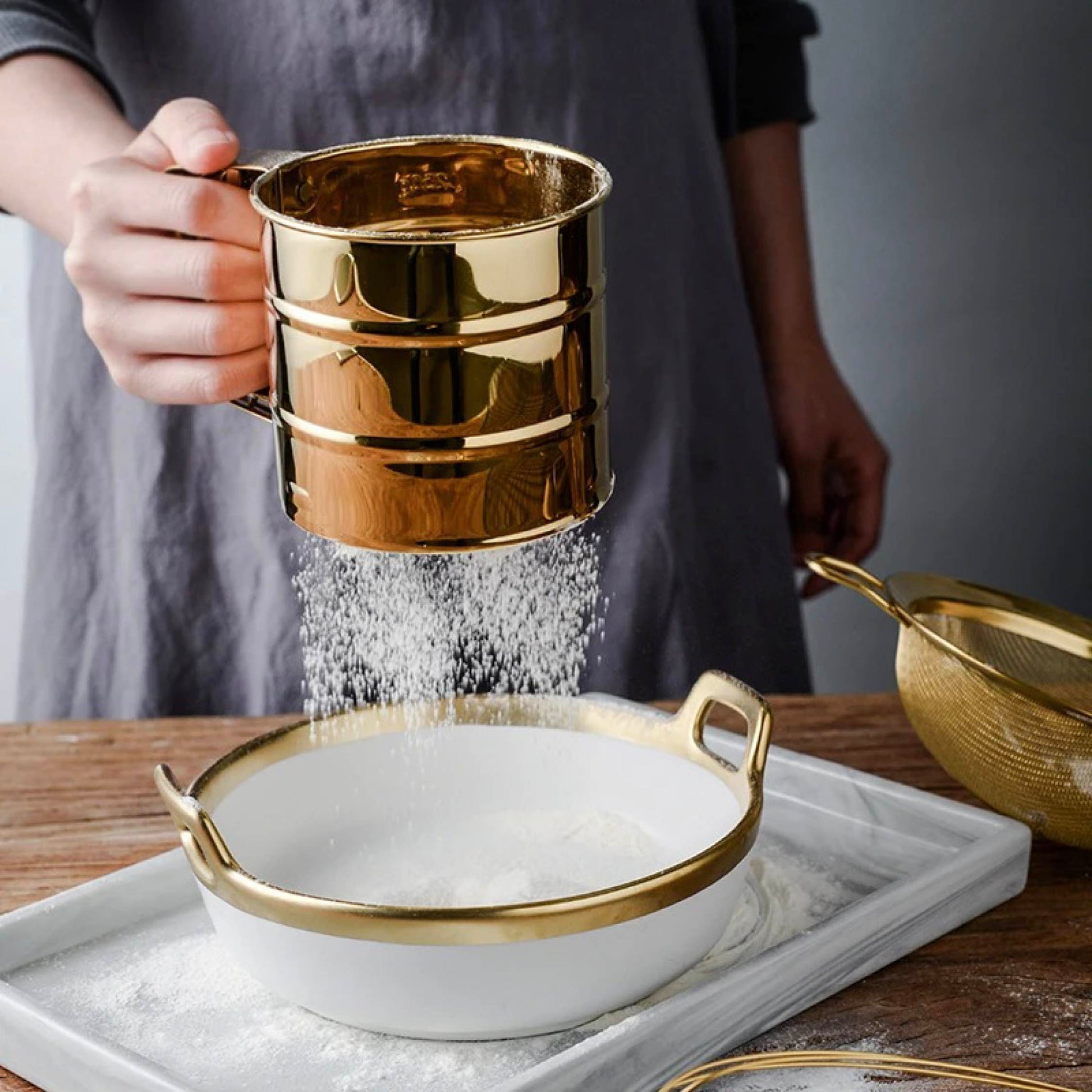 Flour sifter featuring fine mesh and ergonomic crank handle in gold stainless steel