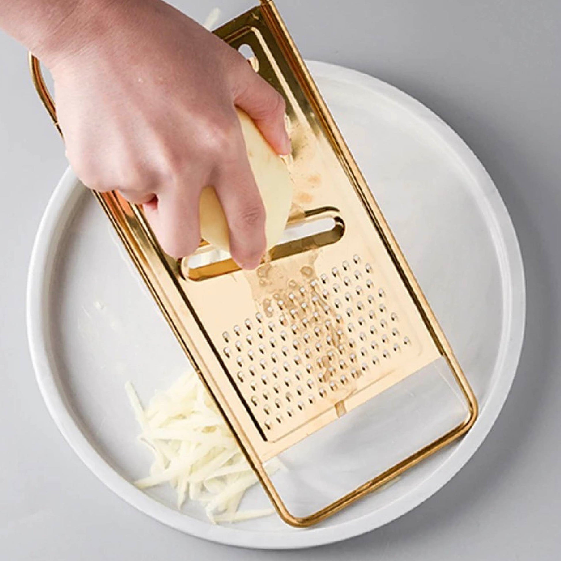 Hand using gold stainless steel grater to grate cheese over a ceramic bowl