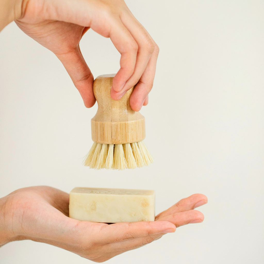Hand holding sisal fiber scrubber above palm to show scale and ergonomic wooden handle
