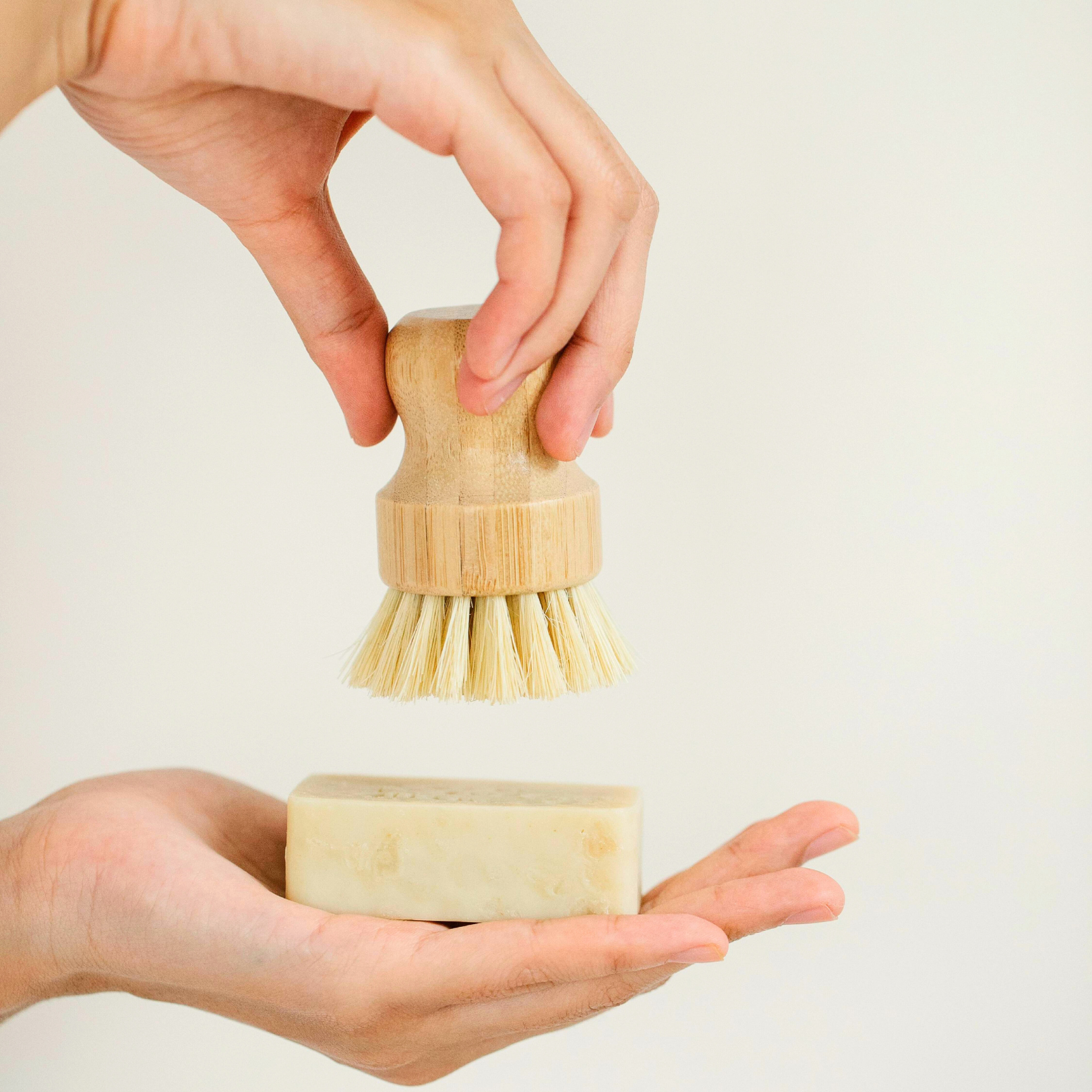 Hand holding sisal fiber scrubber above palm to show scale and ergonomic wooden handle