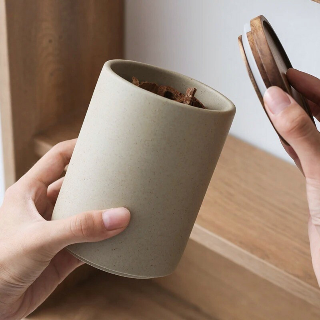 Hand lifting wooden lid off ceramic storage jar, revealing the open container