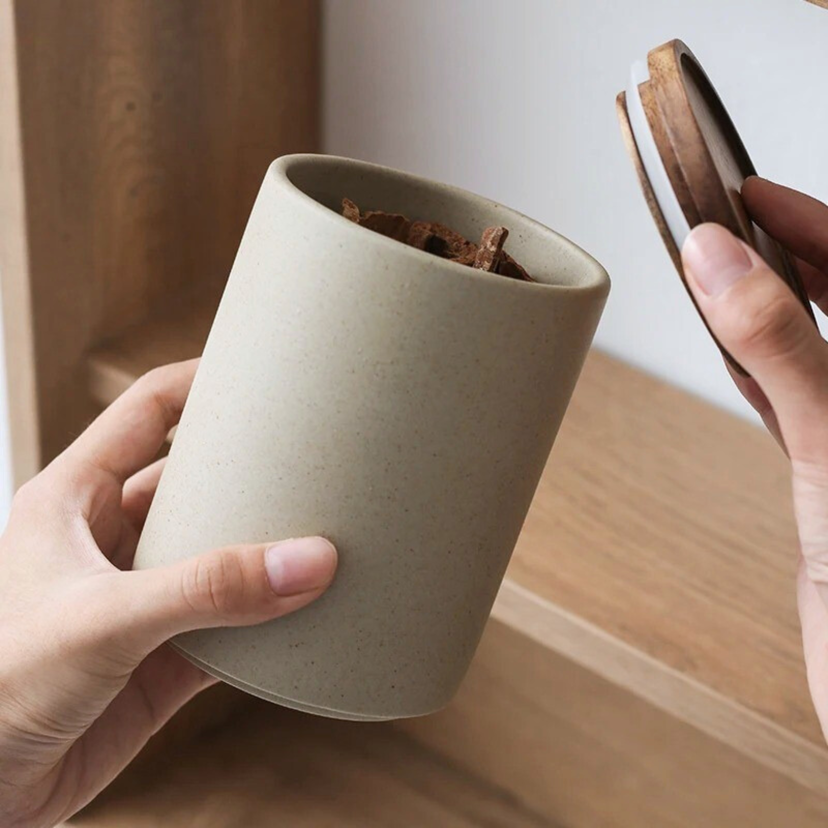 Hand lifting wooden lid off ceramic storage jar, revealing the open container