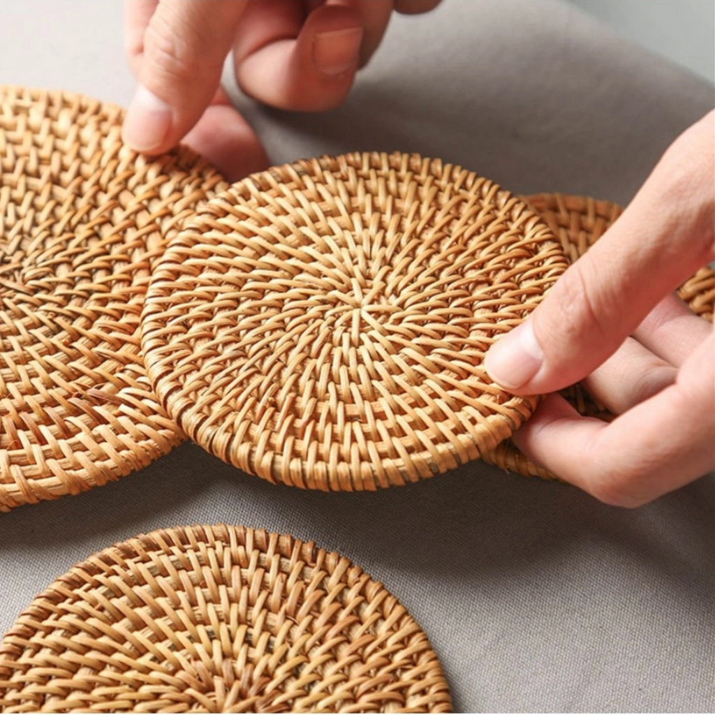 Hand picking up a rattan coaster from a table, with several coasters nearby