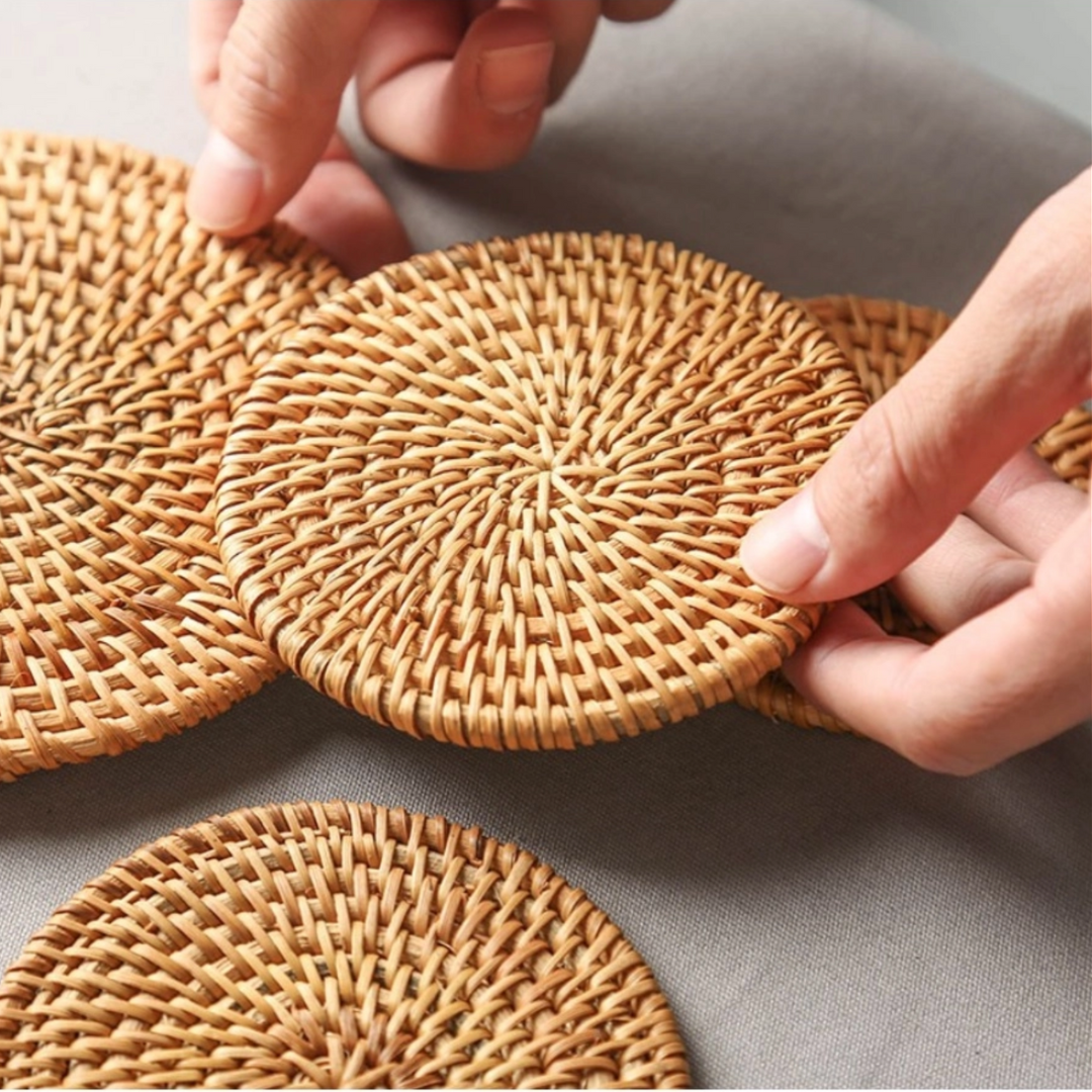 Hand picking up a rattan coaster from a table, with several coasters nearby