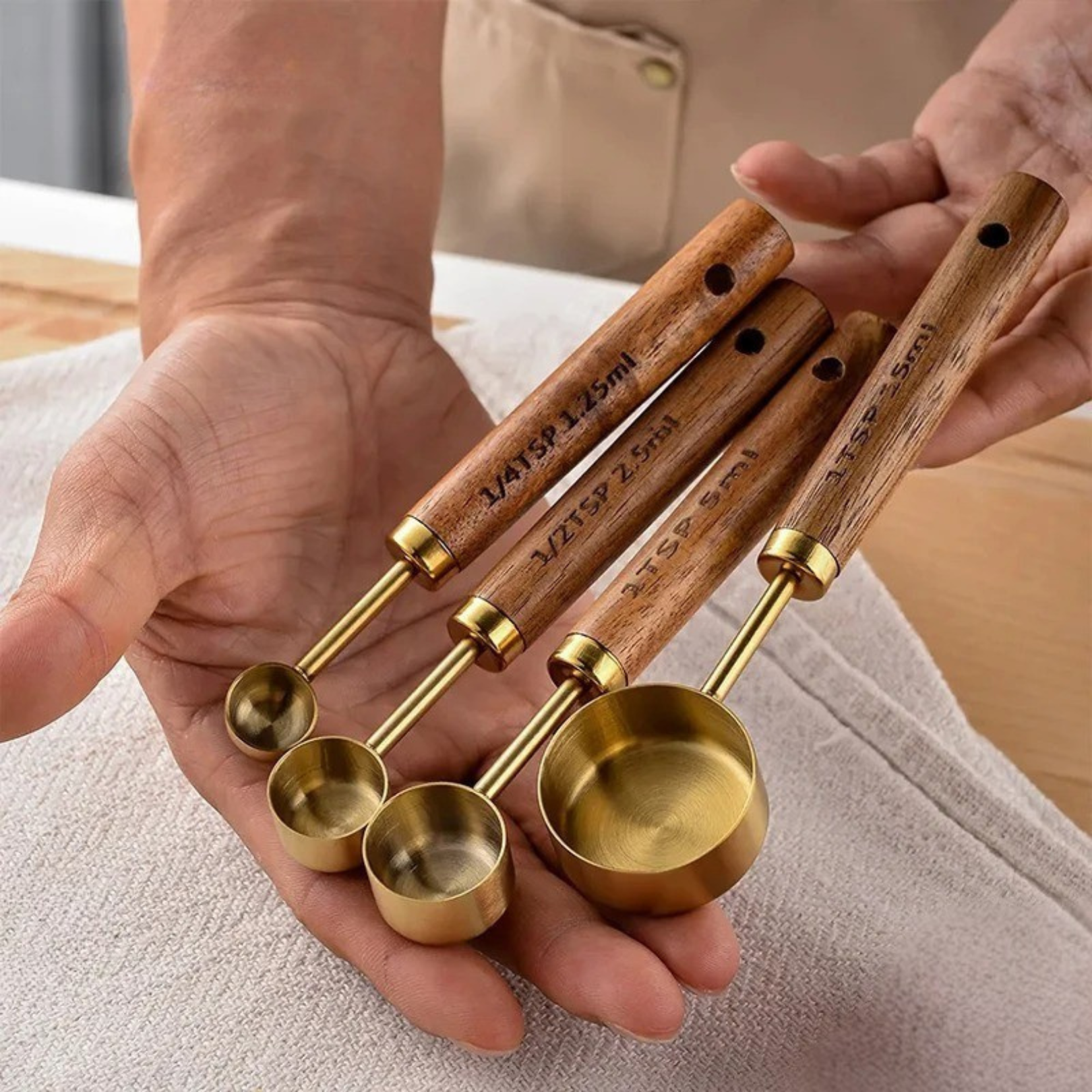 A hand holding all rose gold measuring spoons laid across the palm, showing the full set together
