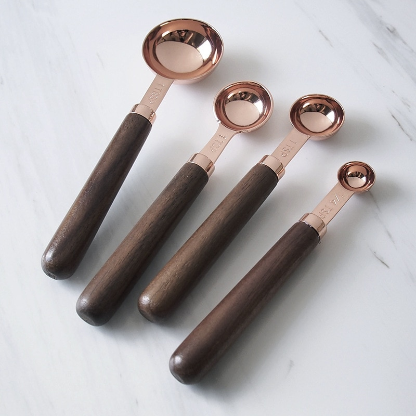 Rose measuring spoons with engraved measurements and wooden handles displayed in a row on a clean marble surface