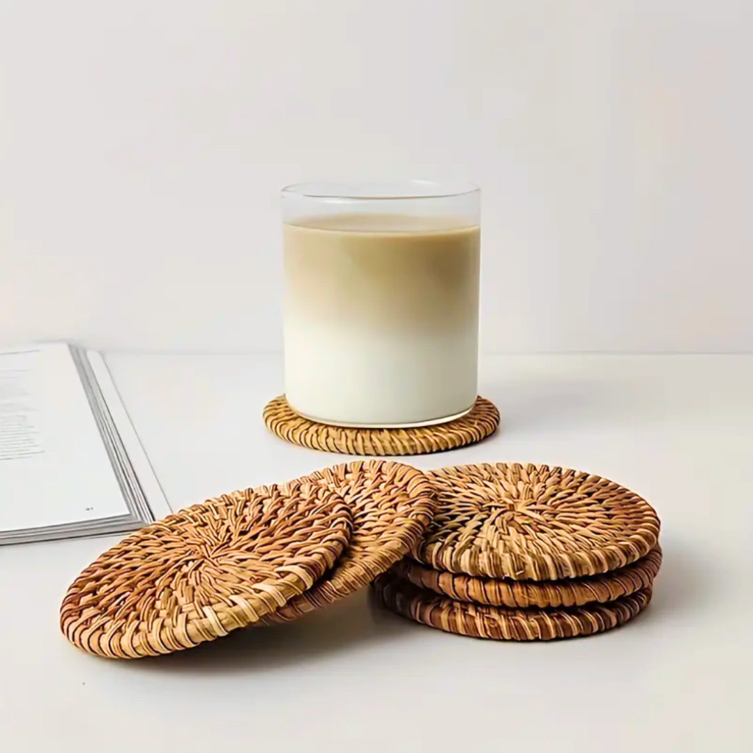 Cup of coffee on wooden table resting on a rattan coaster, with four more coasters casually arranged nearby in a cozy lifestyle setting
