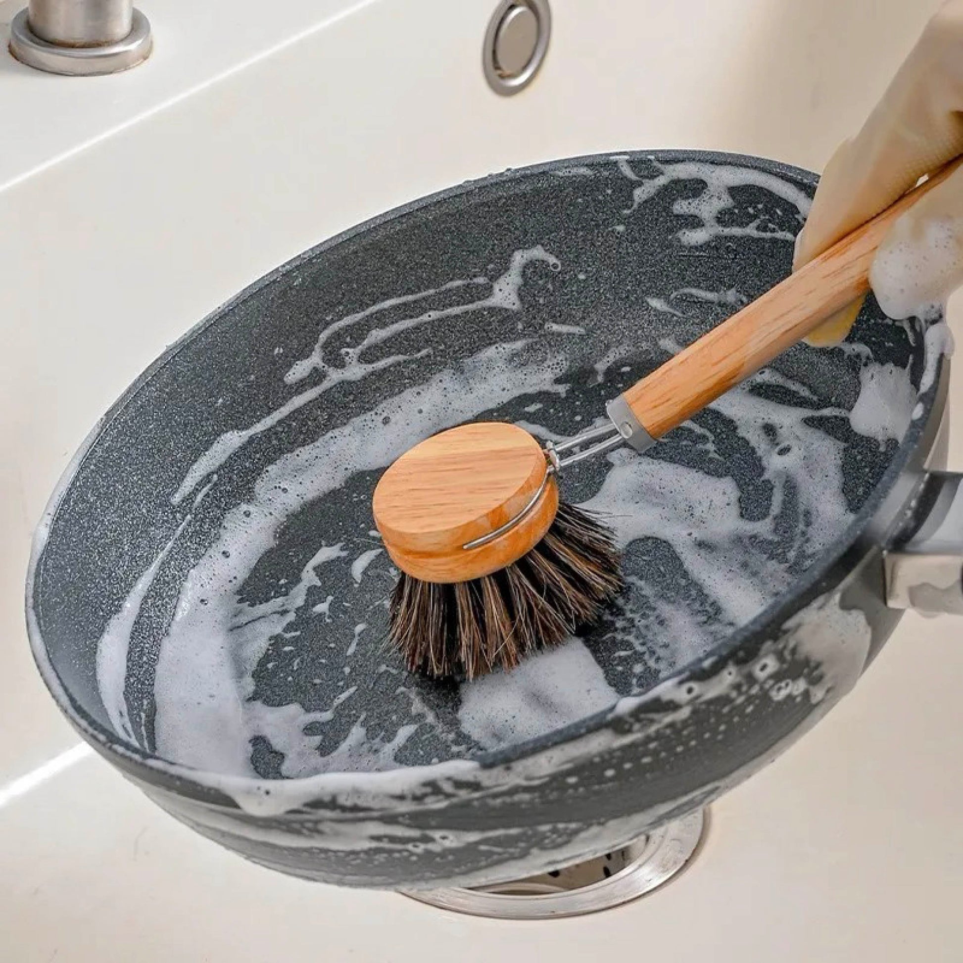 Sisal dish brush with replaceable head scrubbing a grey nonstick pan