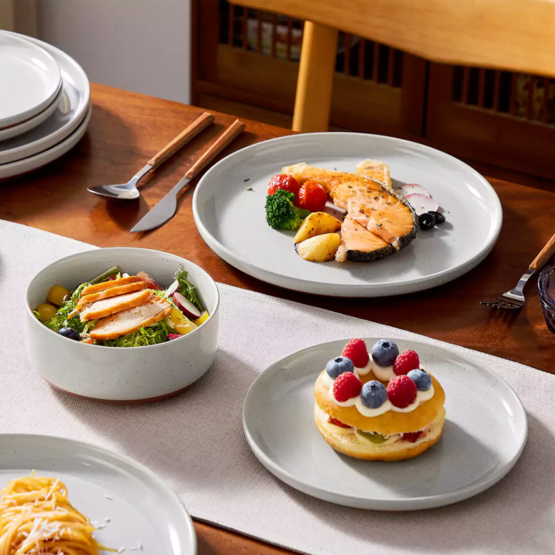 Cool gray stoneware dining set in use with food served in the soup bowl, dessert plate, and dinner plate on a styled dining table