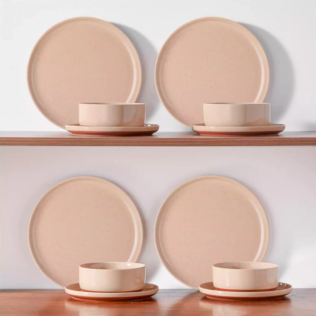 Blush pink stoneware dinnerware neatly arranged on a wooden shelf, showcasing its warm tones and rustic charm