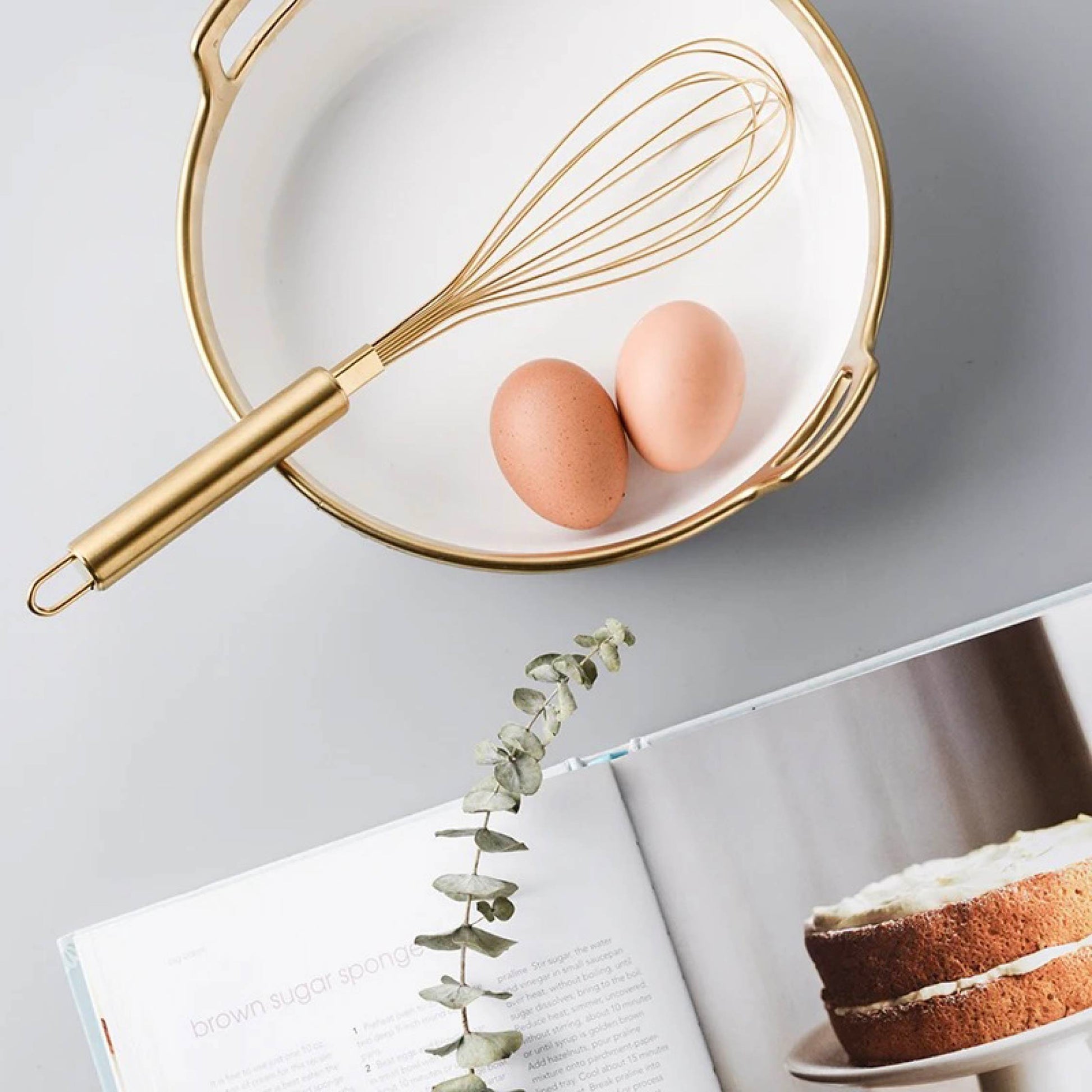 Whisk resting inside a gold-trimmed ceramic bowl on a kitchen counter in a cozy lifestyle setting