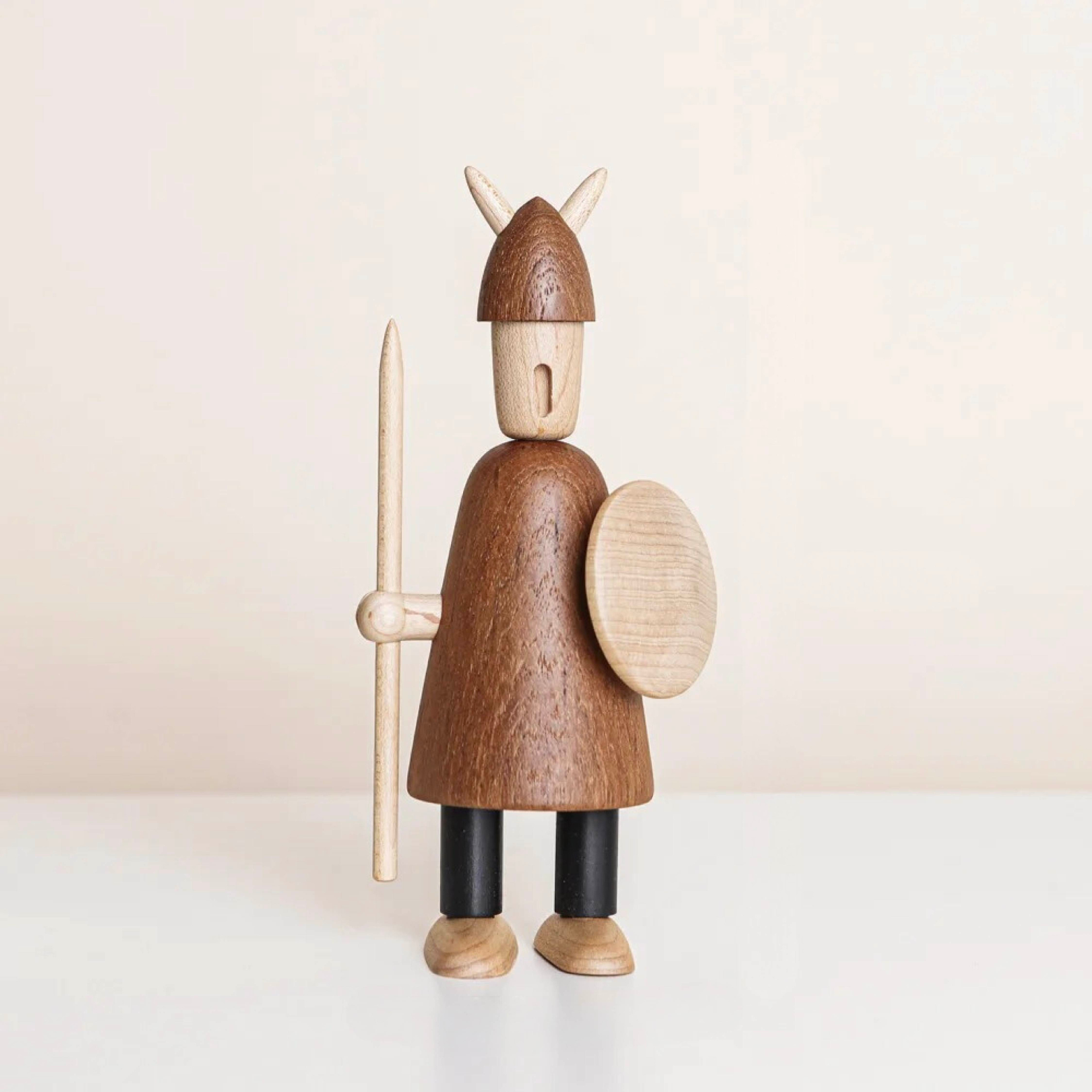 Handcrafted wooden Viking figurine with a shield and upright spear, showing helmet detail